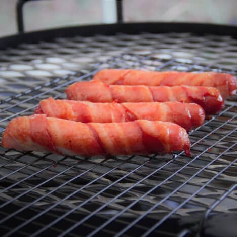 Four bacon-wrapped hot dogs sit on a grill grate.