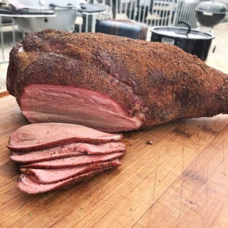 Smoked Leg of Lamb (bone in) sitting on a chopping board with some sliced off to show the smoke ring.