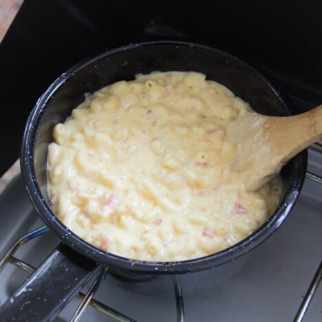 Bacon and onion mac and cheese simmering in a pan over a camp gas stove.