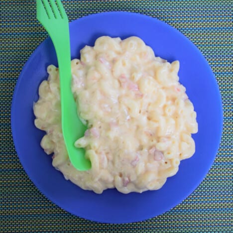 Aerial view of bacon and onion mac and cheese on a blue plate with a green spoon ready to be eaten.