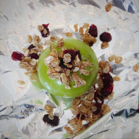 Looking down onto a raw green apple sitting on foil, stuffed with oats and cranberries.