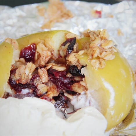 A cooked campfire-baked apple stuffed with oats and dried cranberries with a side of ice cream.