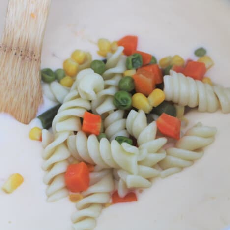 Mixed vegetable and spiral pasta sitting on a cheese sauce in a saucepan.