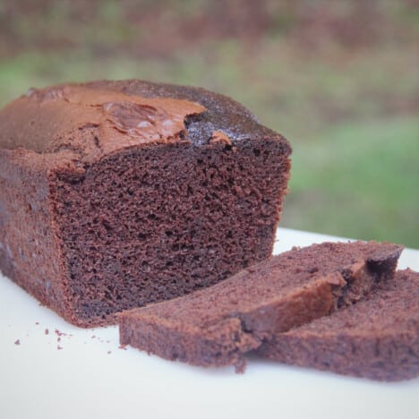 A chocolate cake removed from the tin with two slices removed and resting on a cutting board.