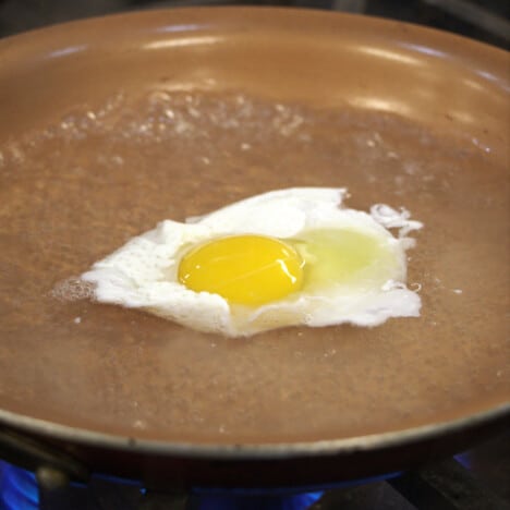 A golden frypan with simmering water poaching an egg.
