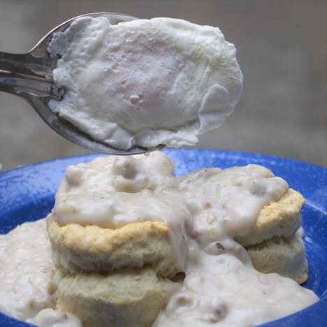 A poached egg being place on biscuits and gravy.