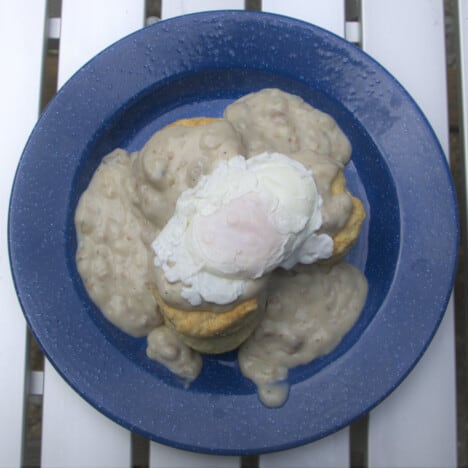 Looking down on a blue camp plate with biscuits, gravy, and a poached egg.
