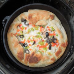 Looking down into a Dutch oven with a stacked pizza inside, with olive and pepper toppings peeking through.