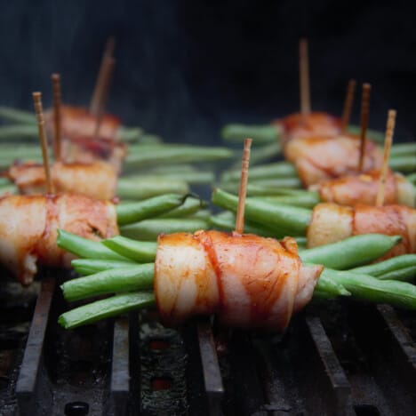 Multiple bacon-wrapped green bean bundles sit on a grill.