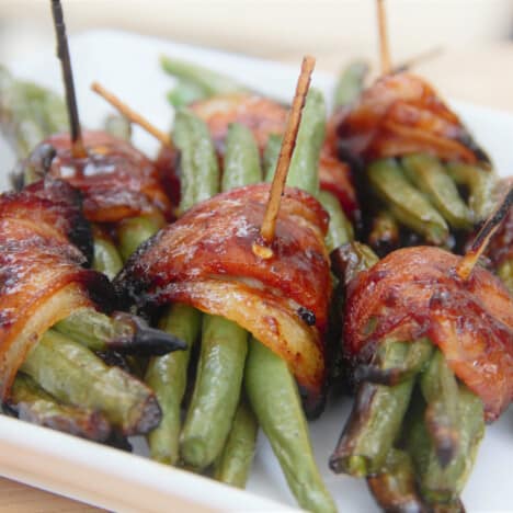 Grilled bacon-wrapped green bean bundles sit on a white serving platter.