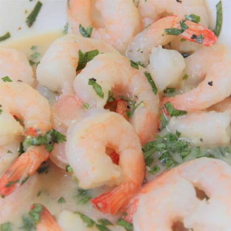 Raw shrimp sitting in a marinade with diced cilantro.