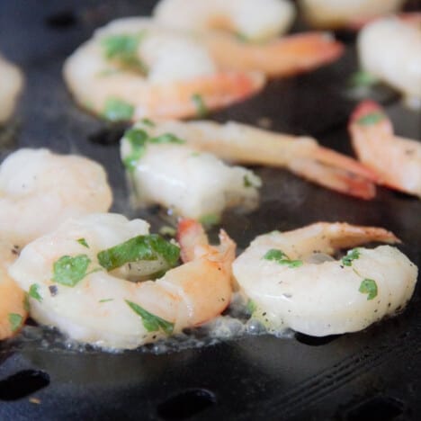 Marinated shrimp cooking on a flat top grill.