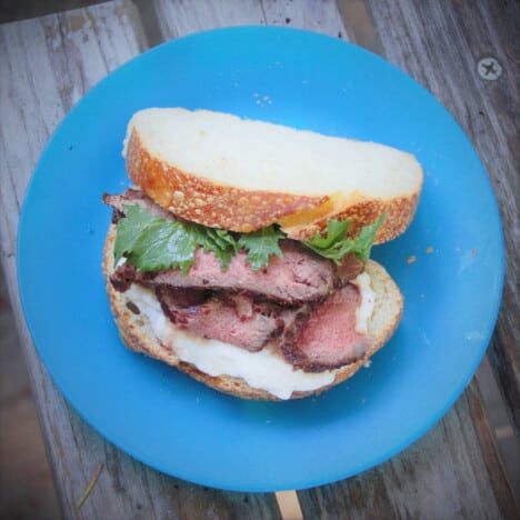 A slightly opened ribeye sandwich sitting on a blue picnic plate.