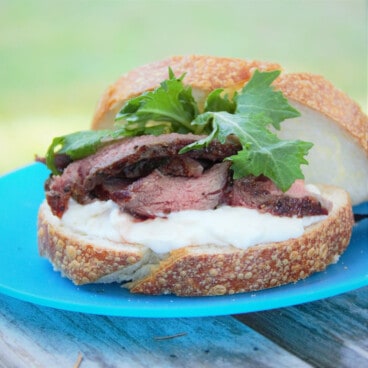 A ribeye sandwich sitting on a blue plastic camp plate.