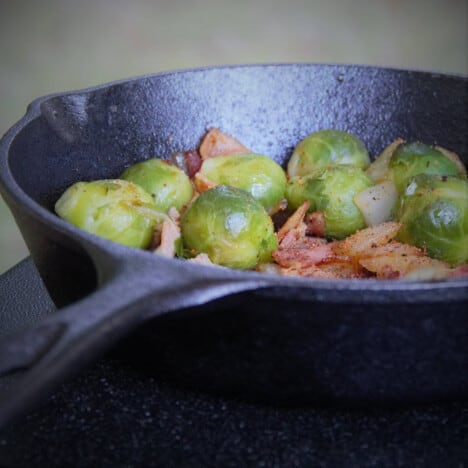 A cast iron skillet with Brussels sprouts, diced onions, and diced bacon in it.