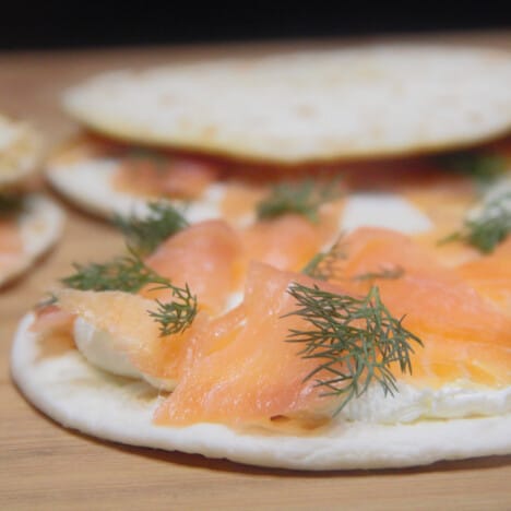 Close up of an open-faced quesadilla on a wooden cutting board with cream cheese, salmon, and dill.