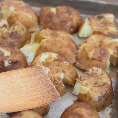 A bamboo spoon is pushing down on cooked potatoes to smash them open.
