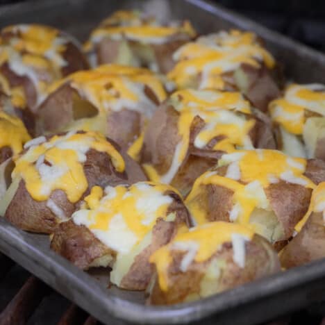 Tray of skin on smashed potatoes topped with melted cheese.