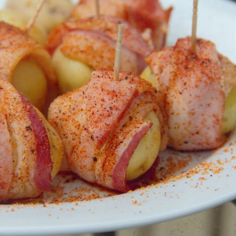 A plate of uncooked baby potatoes wrapped in bacon and secured with a toothpick.