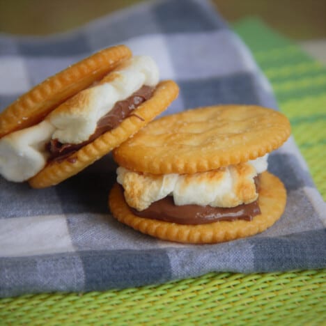 Two cracker smores, one leaning against the other, sit on a blue checkered napkin.