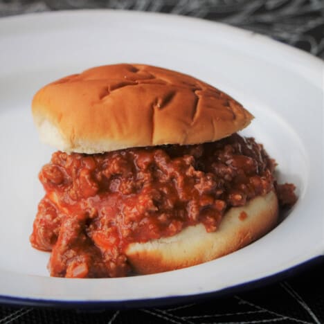 A sloppy joe on a camp plate consisting of ground beef sauce in a burger roll.