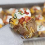A smashed and stuffed potato garnished with sour cream and bacon being lifted from the tray with a spatular.