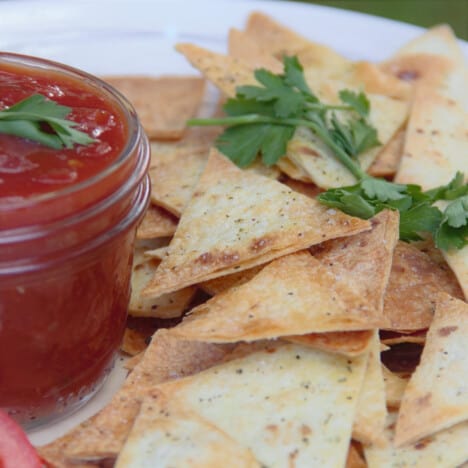 A pile of baked tortilla chips next to a jar of salsa.