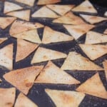Baked tortilla chips spread out on a baking sheet.