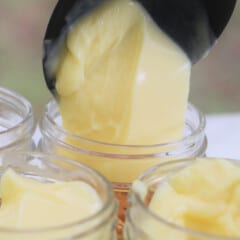 A scoop of set banana pudding being added to a jar surrounded by other banana puddings in jars.