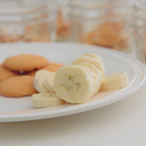 Sliced bananas and vanilla wafers on a white plate with the serving jars in the background.