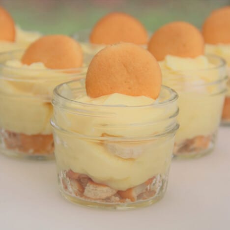 Small jars of banana pudding garnished with a standing vanilla wafer laid out on a table.