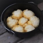 Dumplings sitting in the golden syrup liquid in a Dutch oven.