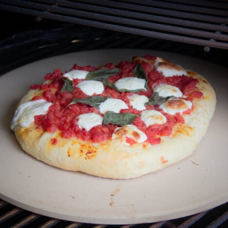 Looking down onto a cooked Margherita pizza on a pizza stone in a closed barbecue.