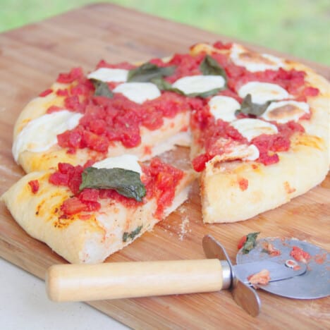A cooked Margherita pizza lays on a wooden cutting board with a slice removed.