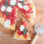 Looking down onto a cooked Margherita pizza on a wooden cutting board with a pizza cutter and one slice removed.
