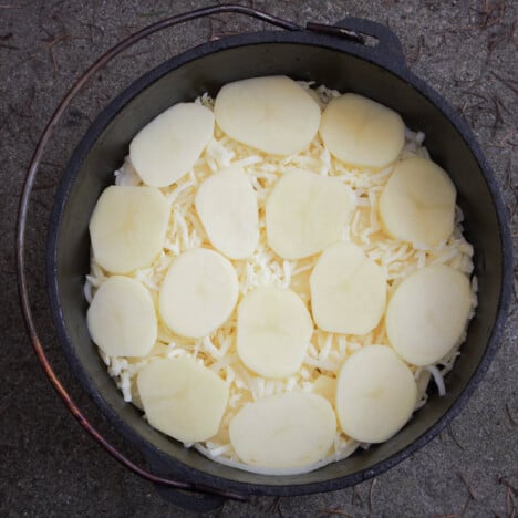 Looking down into a Dutch oven with a layer of sliced potatoes sitting on a layer of onions.