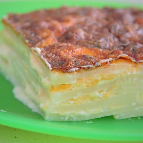 Close up of a slice of potato bake on a green camp plate showing the layers.