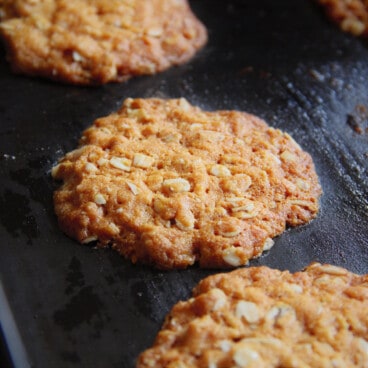 Three baked ANZAC biscuits rest on a baking sheet.