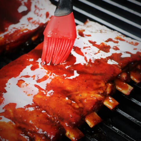 A red basting brush adding a glaze to the cooked ribs.