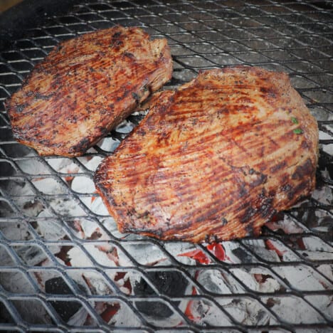 A charcoal grill with two flank steaks cooking on it.