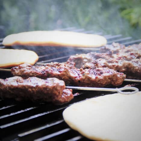 Grilled Beef Kebab skewers cooking on the gill along with pita bread.