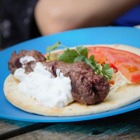 A plate of Grilled Beef Kebabs are served in a pita with accompaniments.