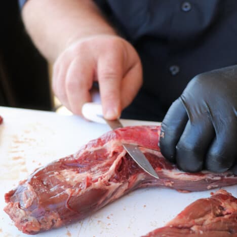 Hanger steak on a white chopping board being trimmed with a butchering knife.