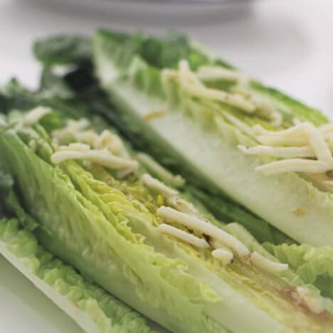 Raw romaine lettuce topped with the seasoned shredded cheese ready to cook.