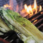 Slightly charred romaine sitting in front of a flaming part of the grill.