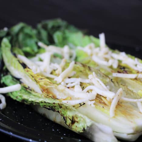 Grilled romaine salad served on a black camp plate and garnished with seasoned cheese.