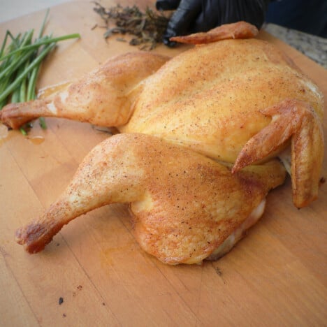 A cooked golden brown butterflied chicken sitting on a wooden chopping board.