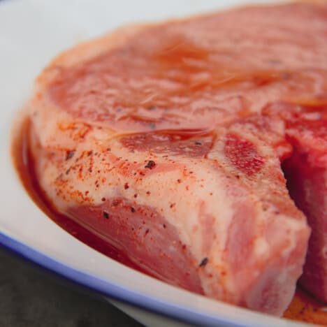 A close up of a pork chop in marinade in a white bowl.