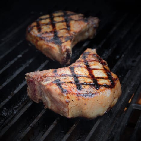 Two large pork chops with deep hatch marks sit on a grill.