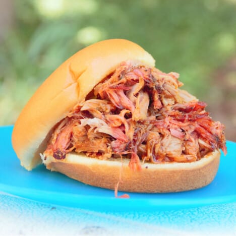 Smoked pork butt is piled on a hamburger bun which rests on a blue plate.